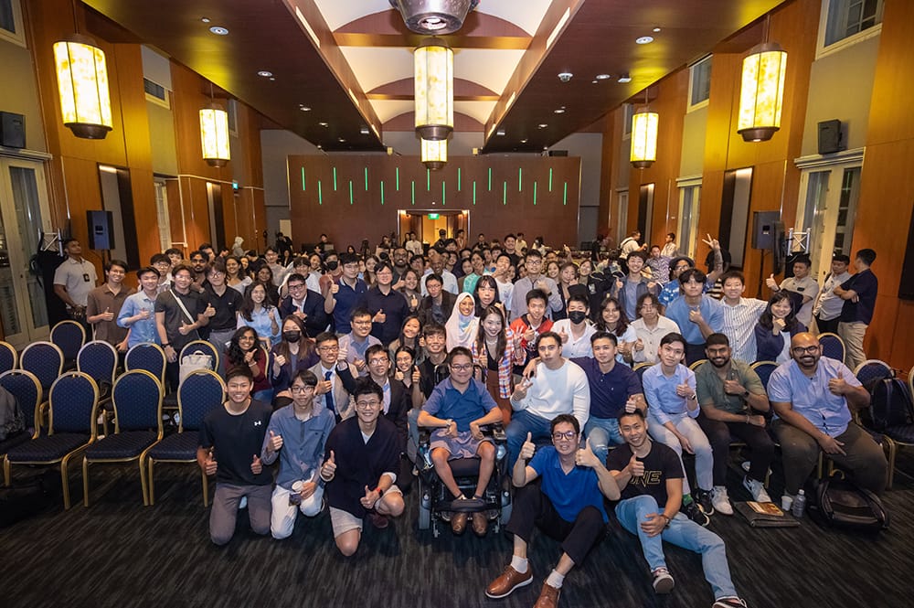 Large group of people in a room, many giving thumbs up.